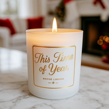 Load image into Gallery viewer, Candle with a label reading &#39;This Time of Year&#39; by Maxine Linehan, lit on a marble surface with a festive background. Scented This Time of Year.
